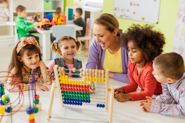 teacher and four children sitting at a table playing with an abacus