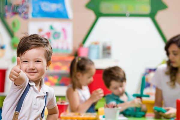 group of children seated at a table with a teacher playing with blocks; little boy giving thumbs up